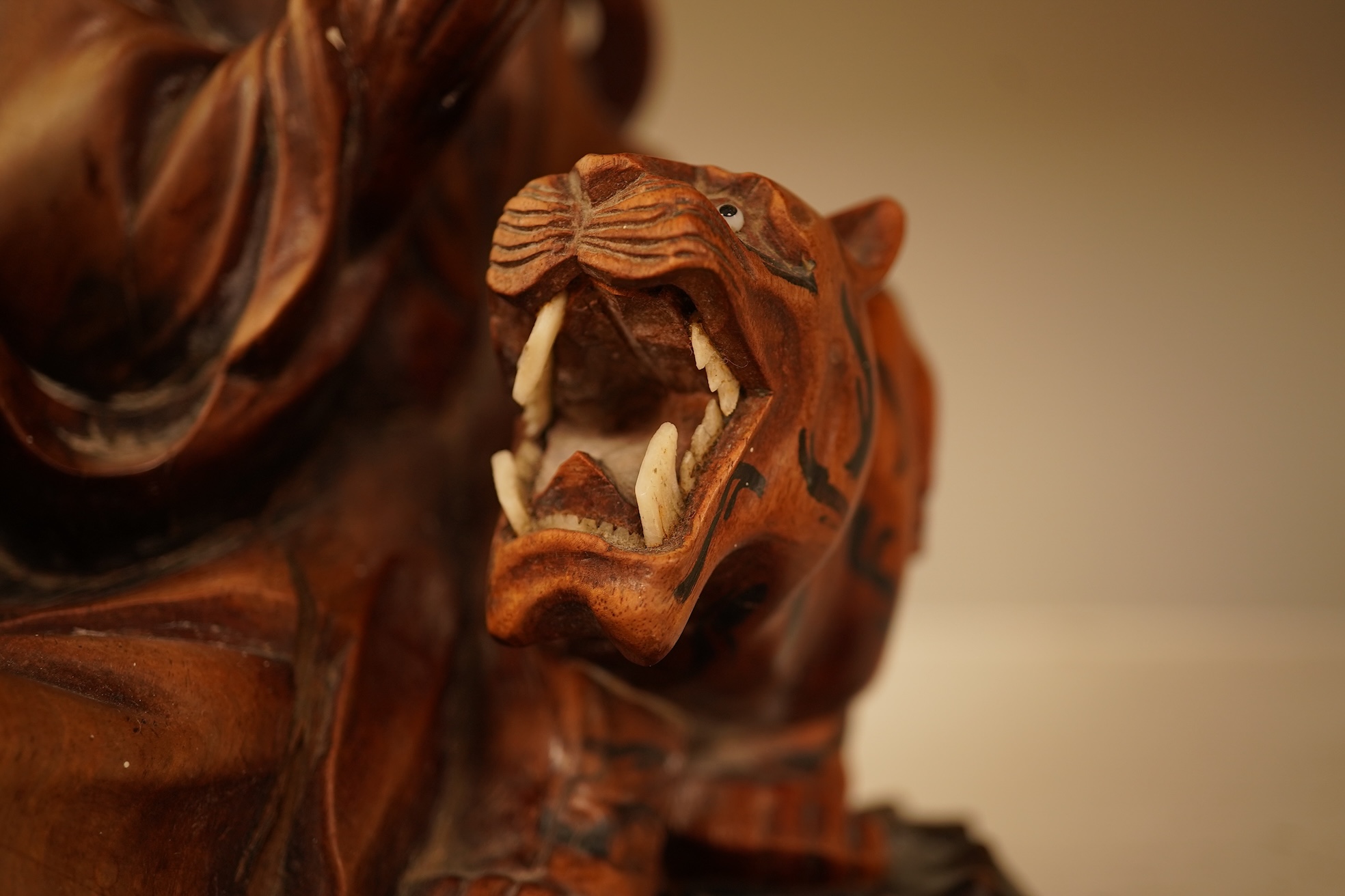 A Chinese hardwood carving of a seated luohan and tiger on hardwood stand, 24cm high including stand.